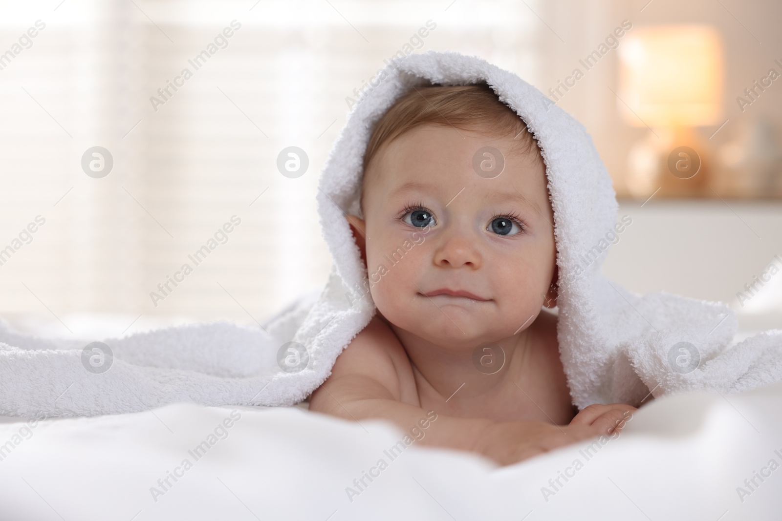 Photo of Cute baby under terry towel lying on bed at home