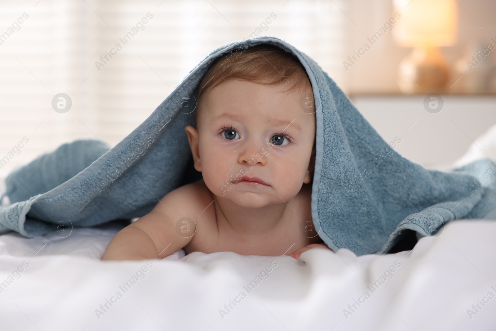 Photo of Cute baby under terry towel lying on bed at home