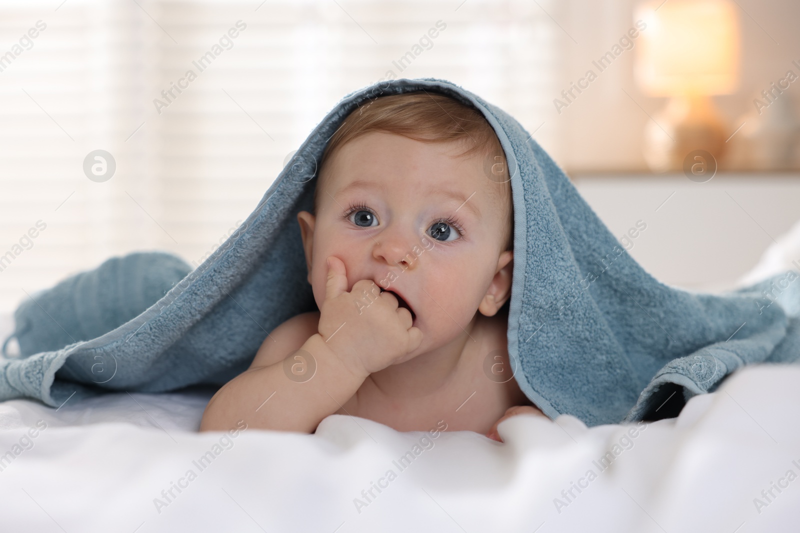 Photo of Cute baby under terry towel lying on bed at home