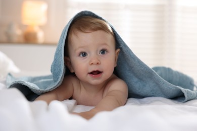 Cute baby under terry towel lying on bed at home