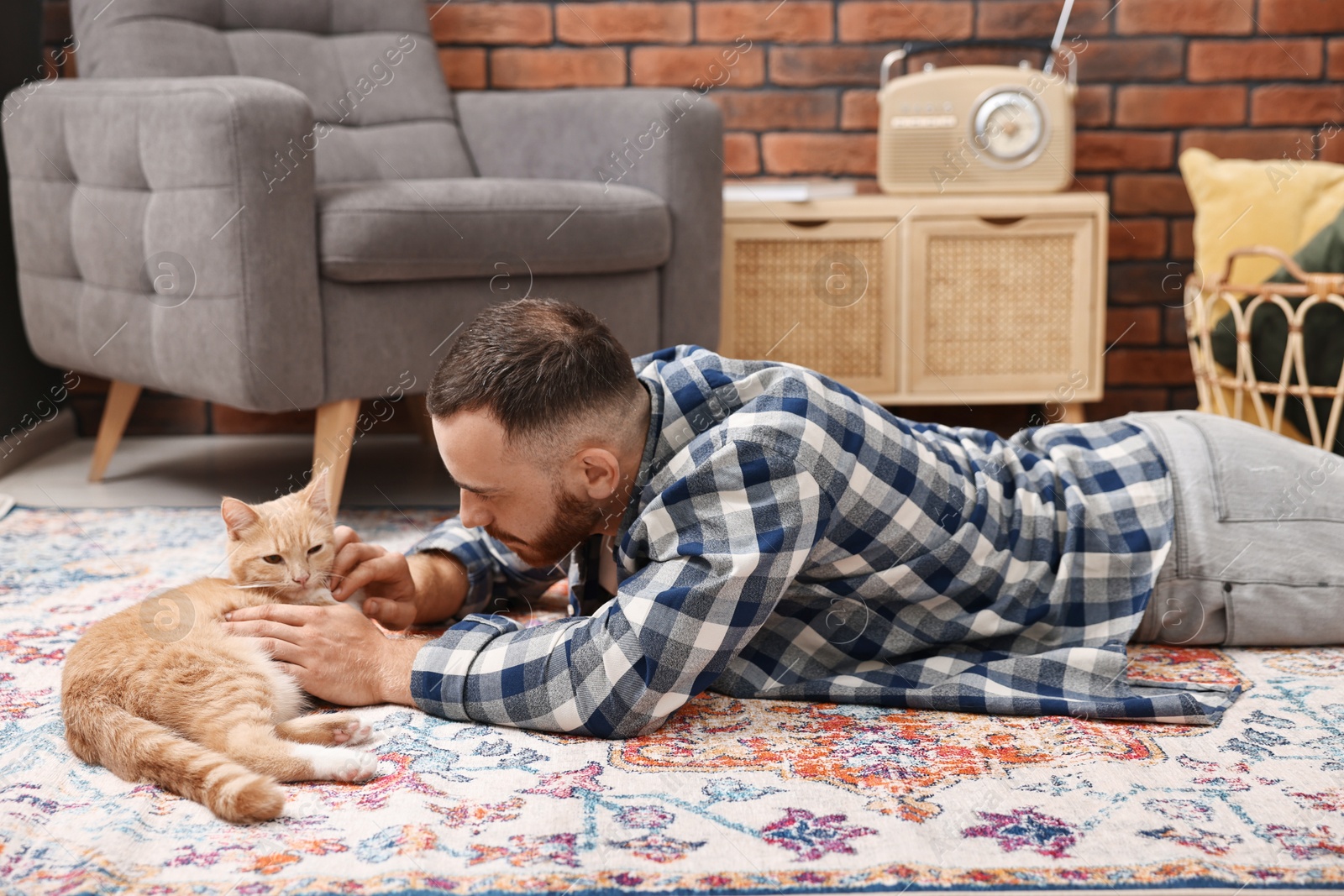 Photo of Man petting cute ginger cat on floor at home