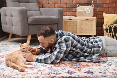 Man petting cute ginger cat on floor at home