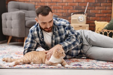 Man petting cute ginger cat on floor at home