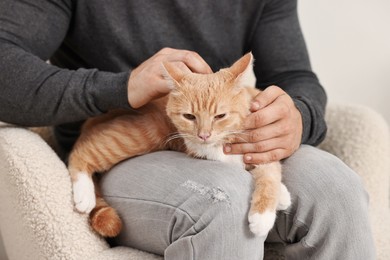 Photo of Man petting cute ginger cat on sofa at home, closeup