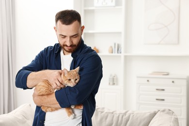 Man petting cute ginger cat at home, space for text