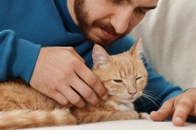 Photo of Man petting cute ginger cat on sofa at home, closeup