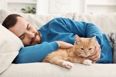 Photo of Man petting cute ginger cat on sofa at home