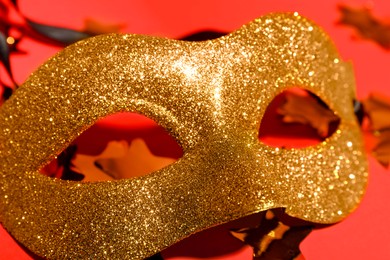 Photo of Beautiful golden carnival mask and confetti on red background, closeup