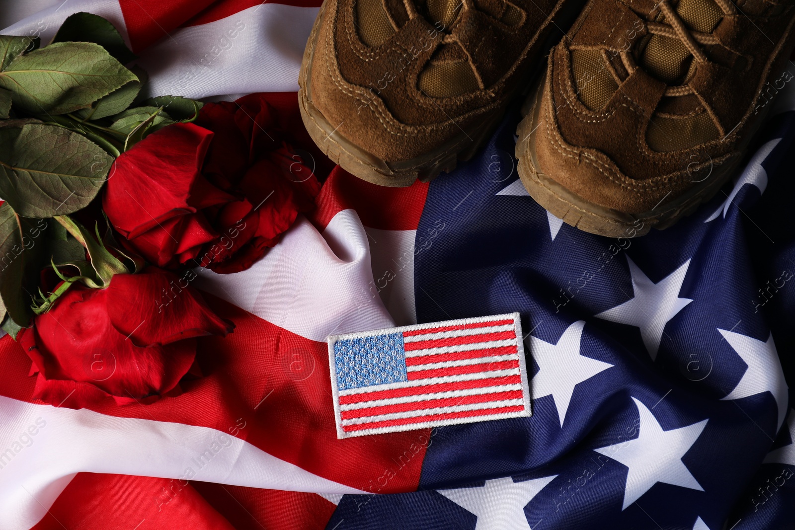 Photo of Veterans day. USA army patch, roses and military shoes on American flag, flat lay