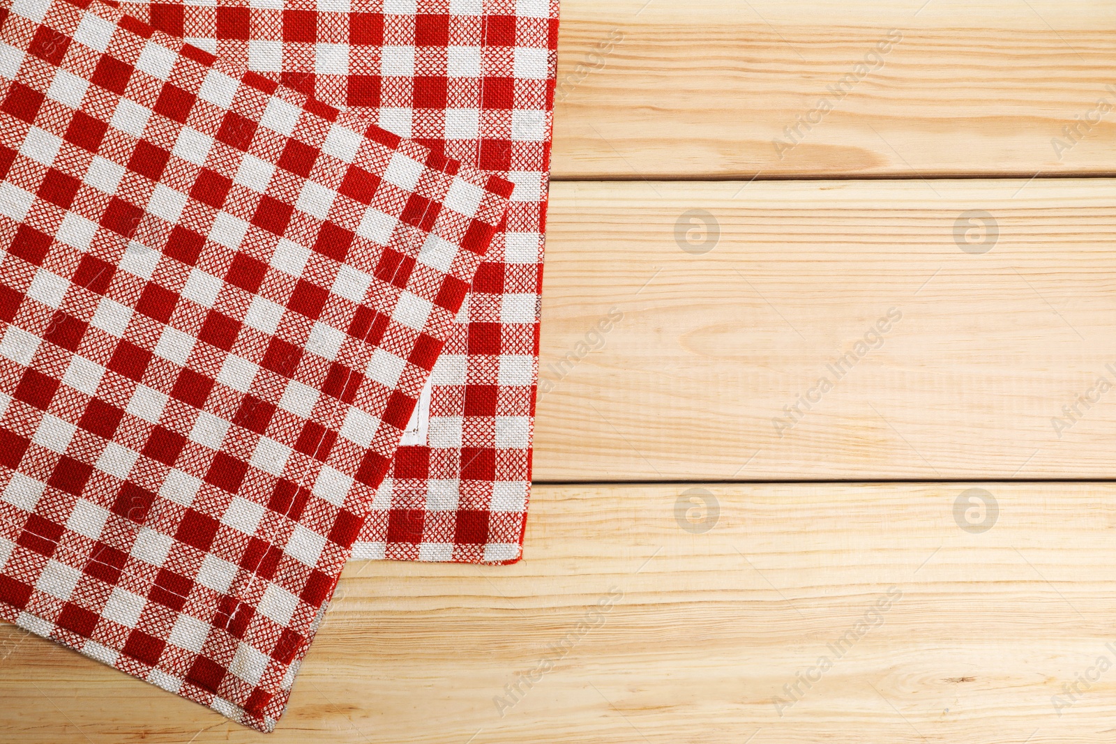 Photo of Folded tablecloth with checkered pattern on light wooden table, top view. Space for text