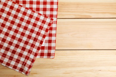 Folded tablecloth with checkered pattern on light wooden table, top view. Space for text