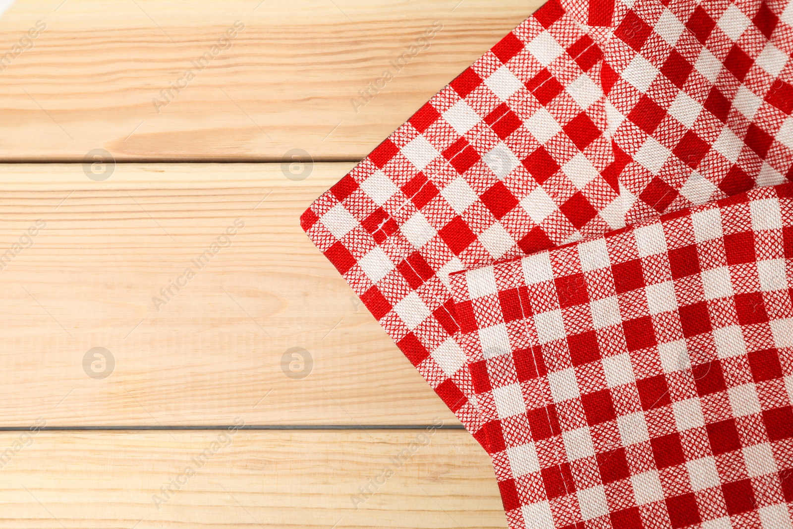 Photo of Folded tablecloth with checkered pattern on light wooden table, top view. Space for text