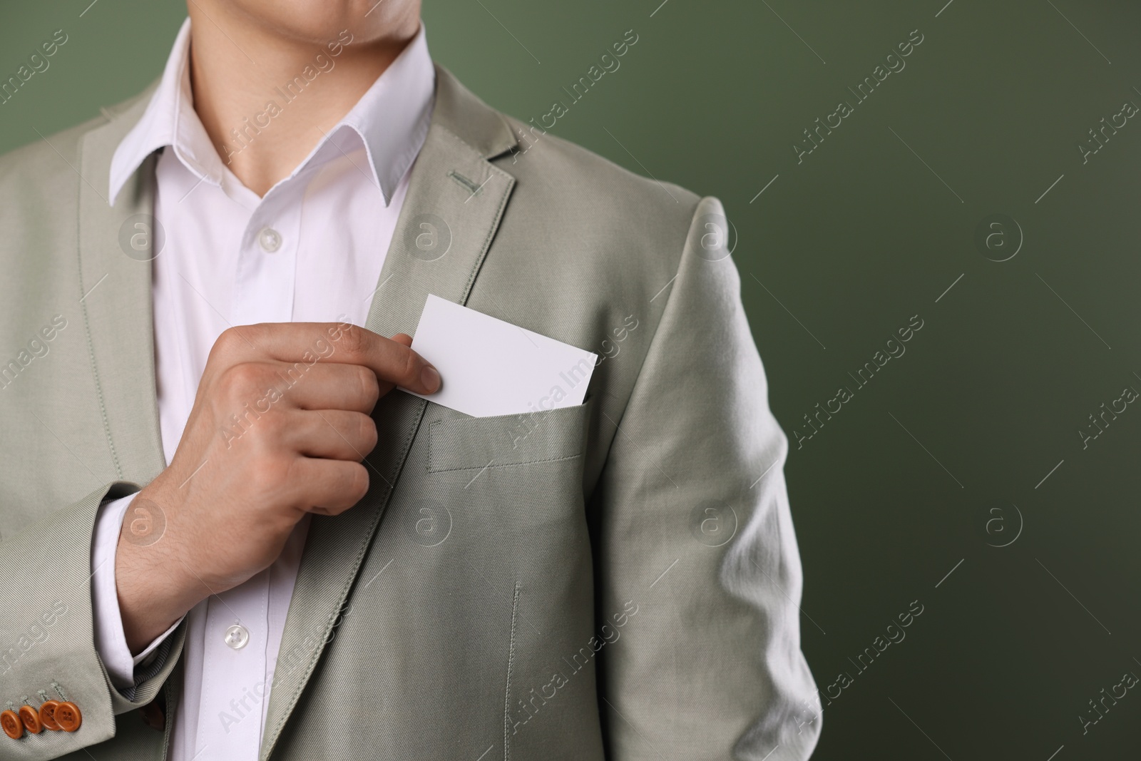 Photo of Man taking blank business card from pocket of his jacket on green background, closeup. Mockup for design