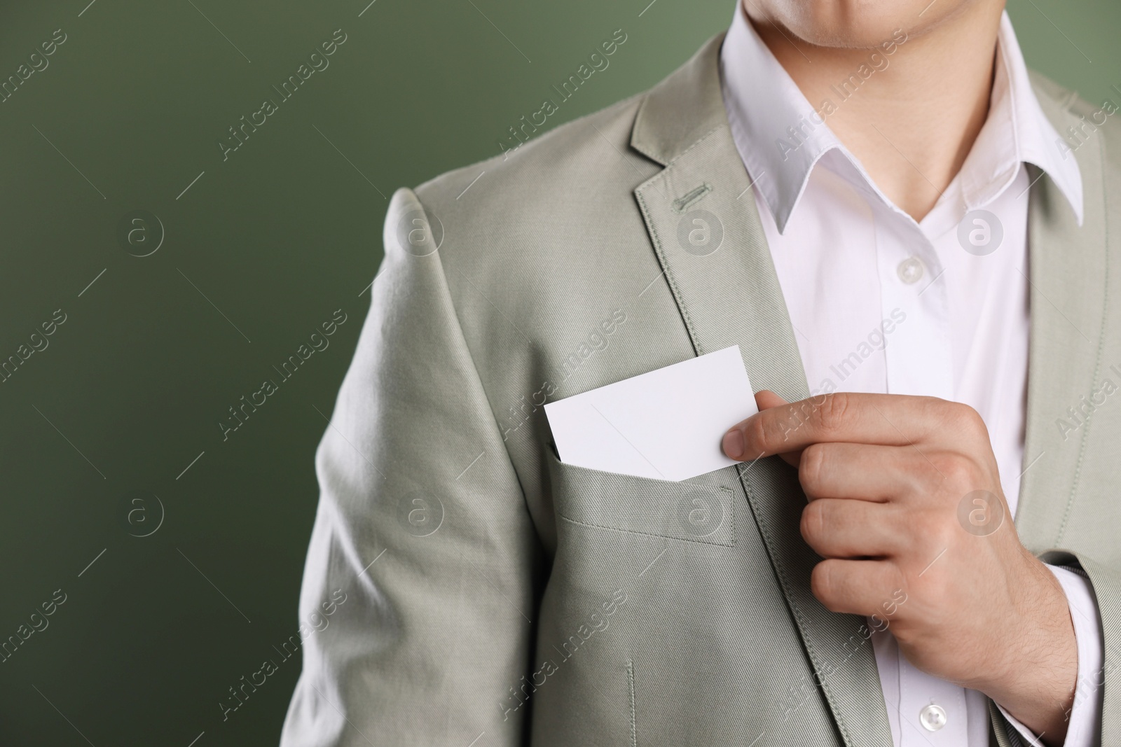 Photo of Man taking blank business card from pocket of his jacket on green background, closeup. Mockup for design