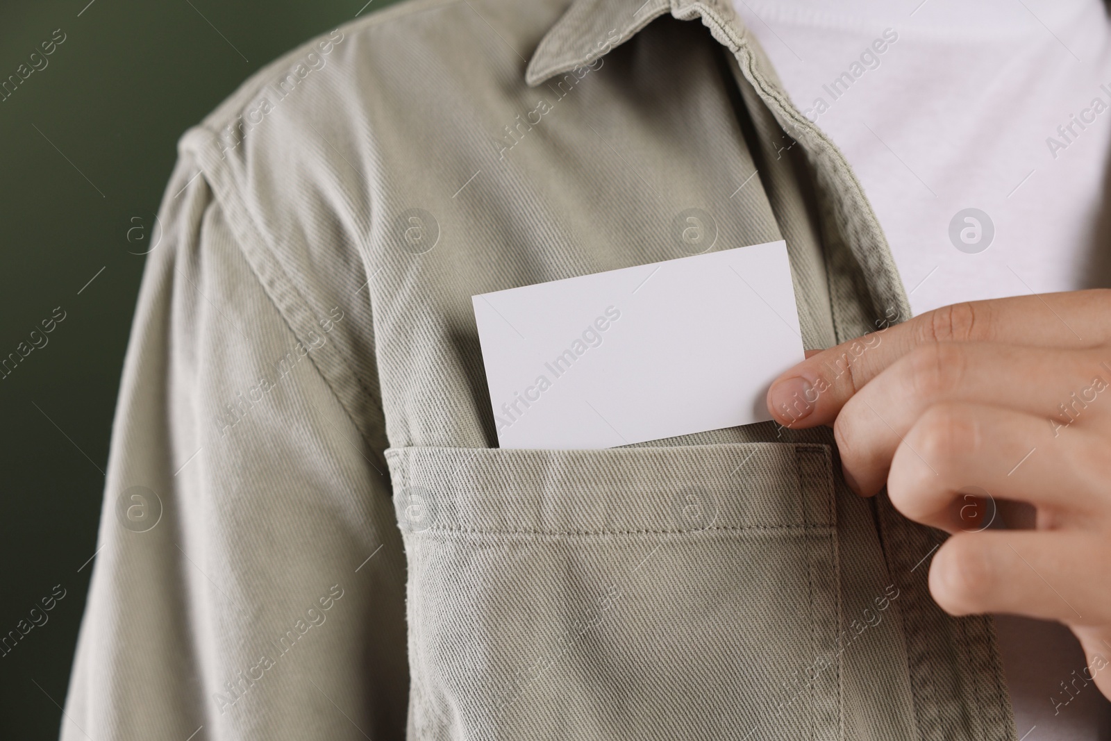 Photo of Man taking blank business card from pocket of his jacket on green background, closeup. Mockup for design