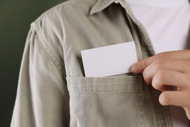 Man taking blank business card from pocket of his jacket on green background, closeup. Mockup for design