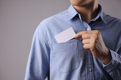 Man taking blank business card from pocket of his jacket on grey background, closeup. Mockup for design