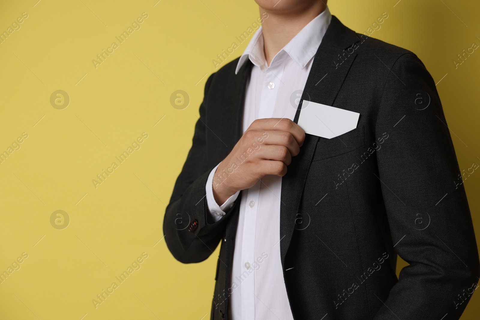 Photo of Man taking blank business card from pocket of his jacket on yellow background, closeup. Mockup for design