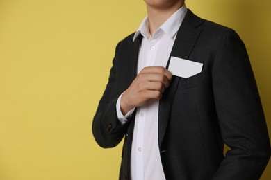 Photo of Man taking blank business card from pocket of his jacket on yellow background, closeup. Mockup for design