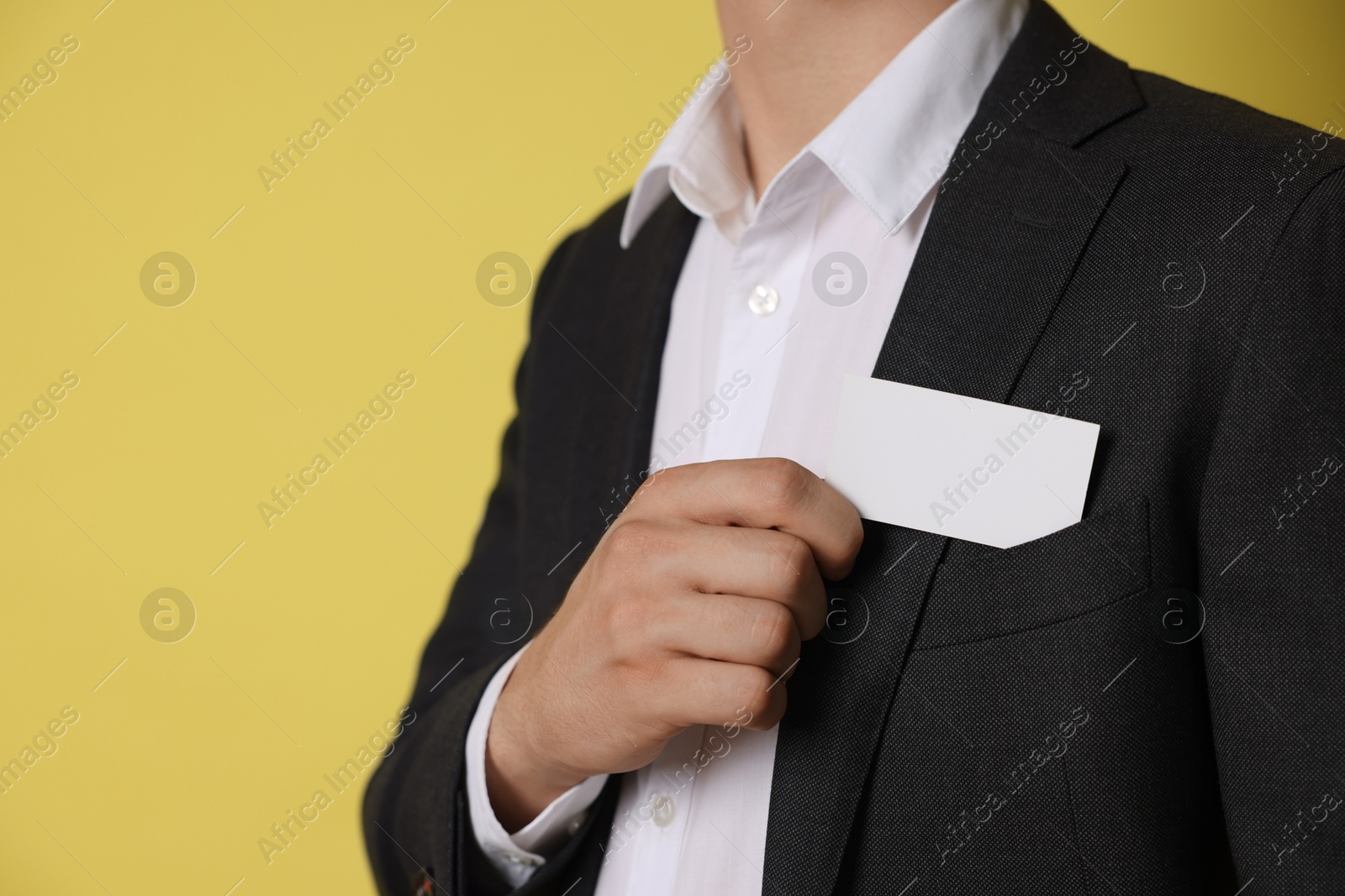 Photo of Man taking blank business card from pocket of his jacket on yellow background, closeup. Mockup for design