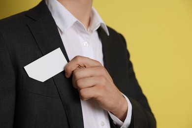 Man taking blank business card from pocket of his jacket on yellow background, closeup. Mockup for design