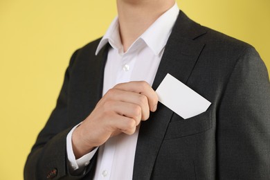 Photo of Man taking blank business card from pocket of his jacket on yellow background, closeup. Mockup for design