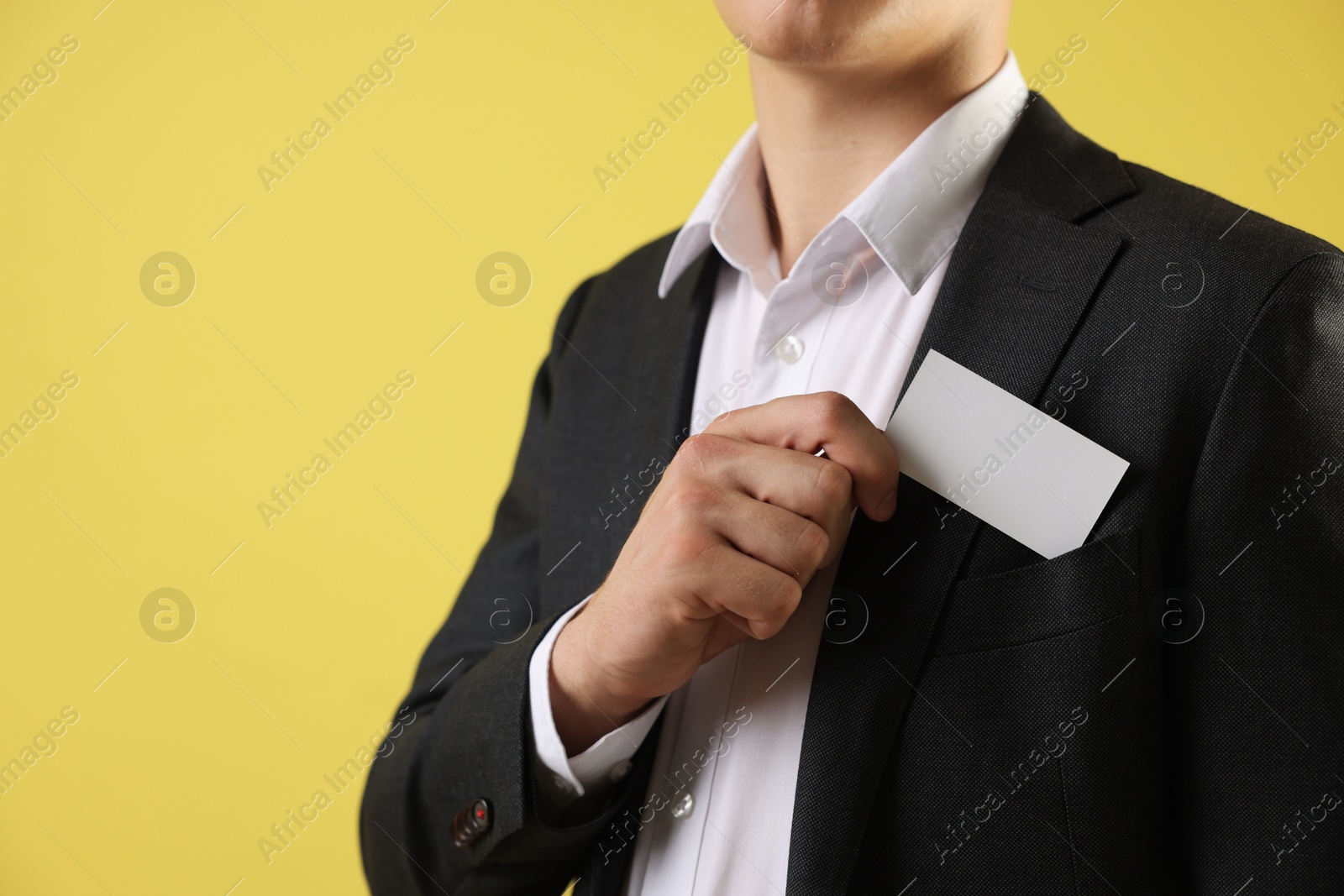 Photo of Man taking blank business card from pocket of his jacket on yellow background, closeup. Mockup for design