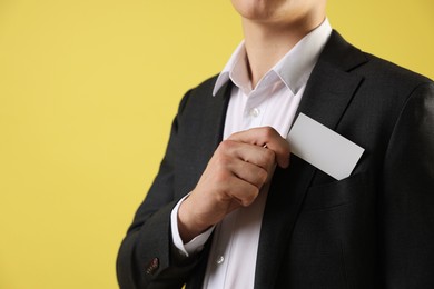 Photo of Man taking blank business card from pocket of his jacket on yellow background, closeup. Mockup for design