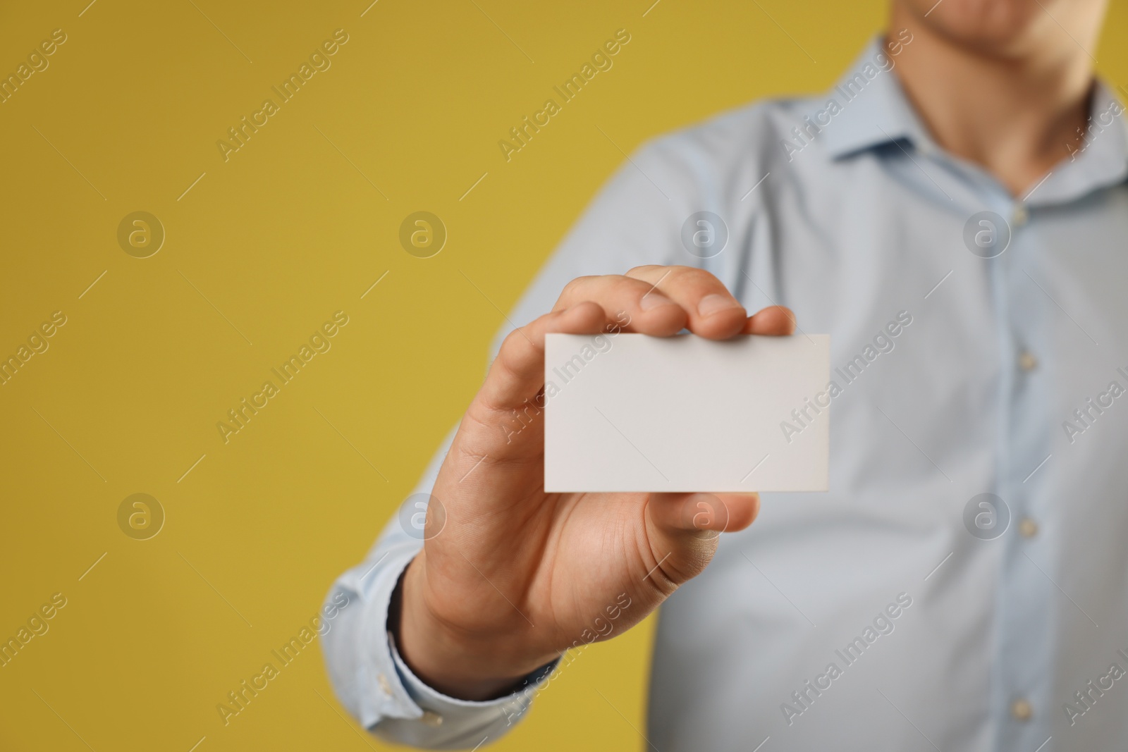 Photo of Man holding blank business card on yellow background, closeup. Mockup for design