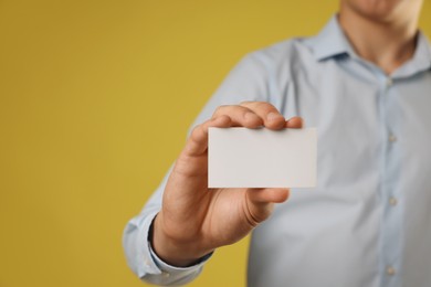 Man holding blank business card on yellow background, closeup. Mockup for design