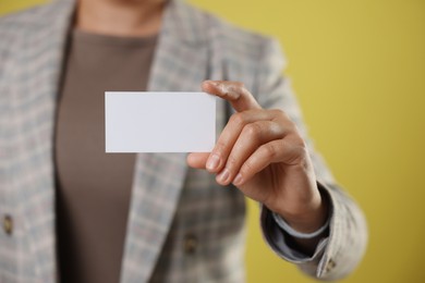 Woman holding blank business card on yellow background, closeup. Mockup for design