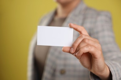 Woman holding blank business card on yellow background, closeup. Mockup for design