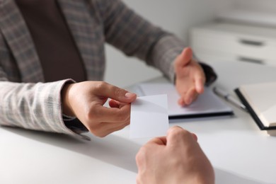 Woman giving business card to man at table in office, closeup. Mockup for design