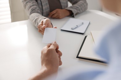 Photo of Woman giving business card to man at table in office, closeup. Mockup for design