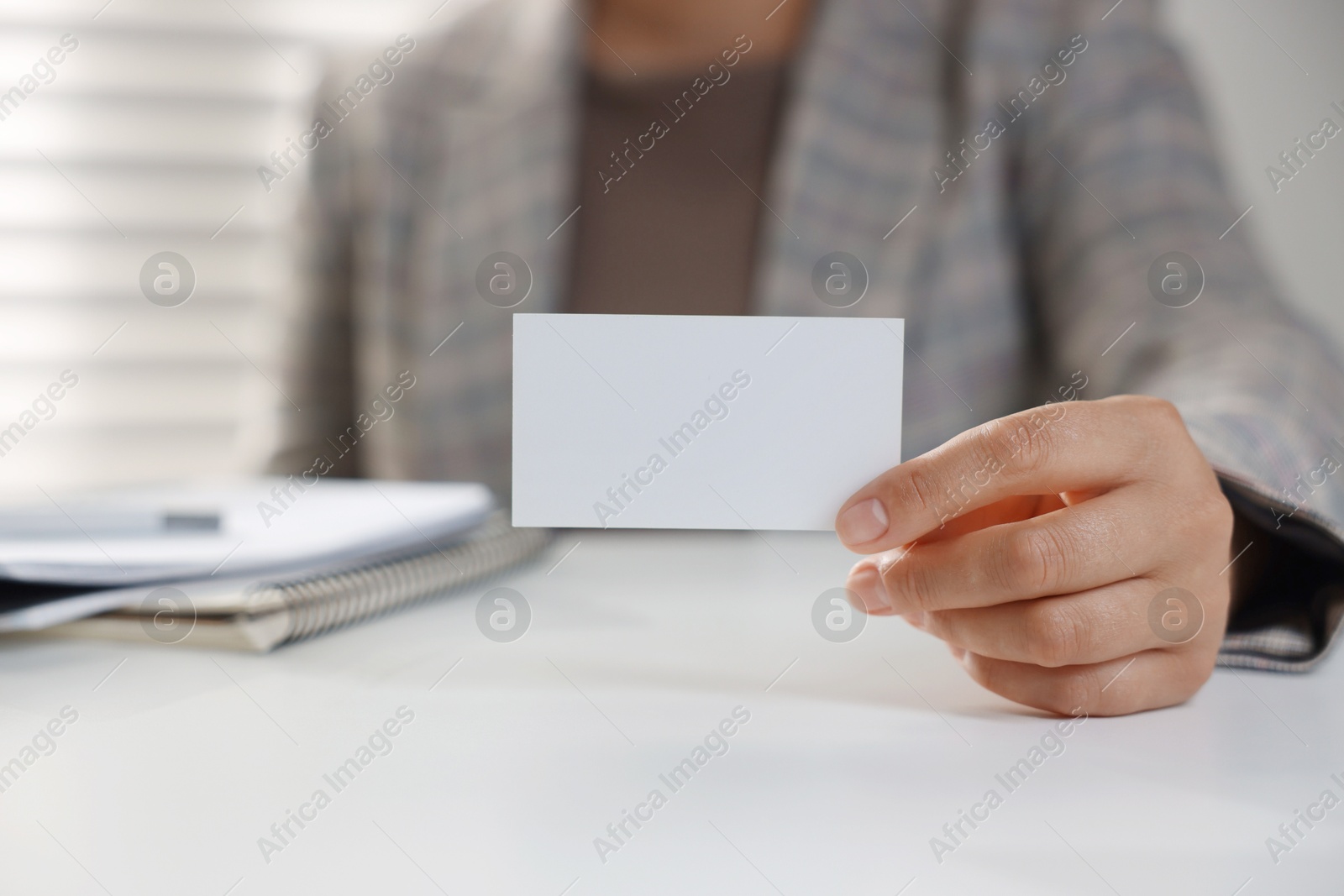 Photo of Woman holding blank business card at table in office, closeup. Mockup for design