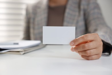 Woman holding blank business card at table in office, closeup. Mockup for design