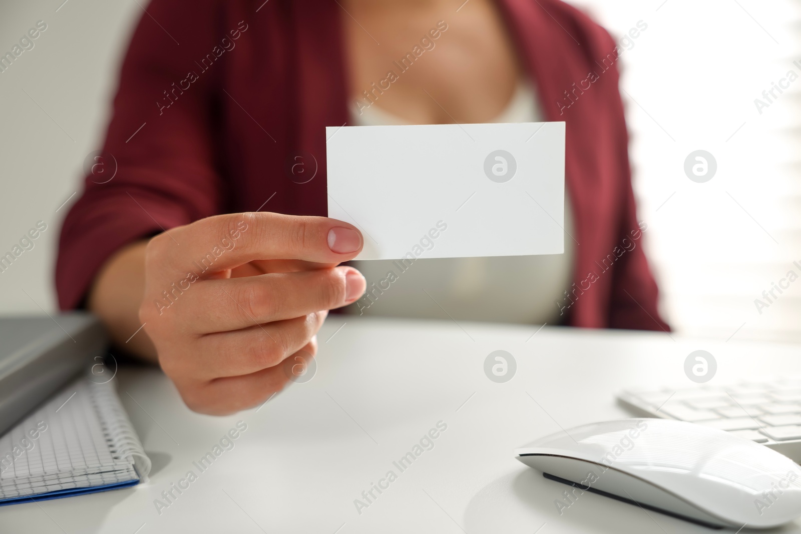 Photo of Woman holding blank business card at table in office, closeup. Mockup for design