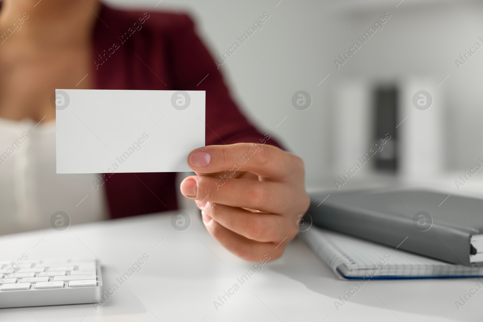 Photo of Woman holding blank business card at table in office, closeup. Mockup for design