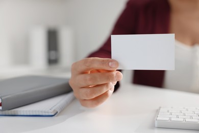 Photo of Woman holding blank business card at table in office, closeup. Mockup for design