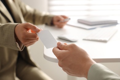 Woman giving business card to man at table in office, closeup. Mockup for design