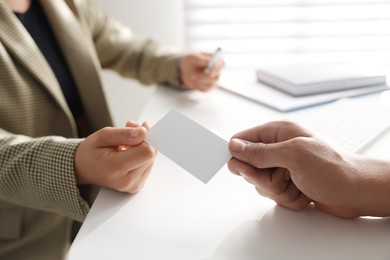 Photo of Woman giving business card to man at table in office, closeup. Mockup for design