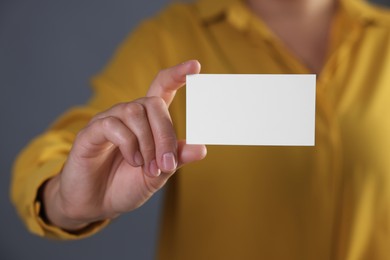 Woman holding blank business card on grey background, closeup. Mockup for design