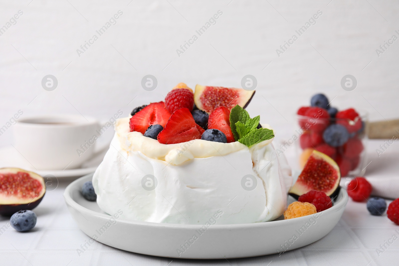 Photo of Pavlova cake (meringue dessert) with whipped cream, fresh berries, mint and fig on white table, closeup