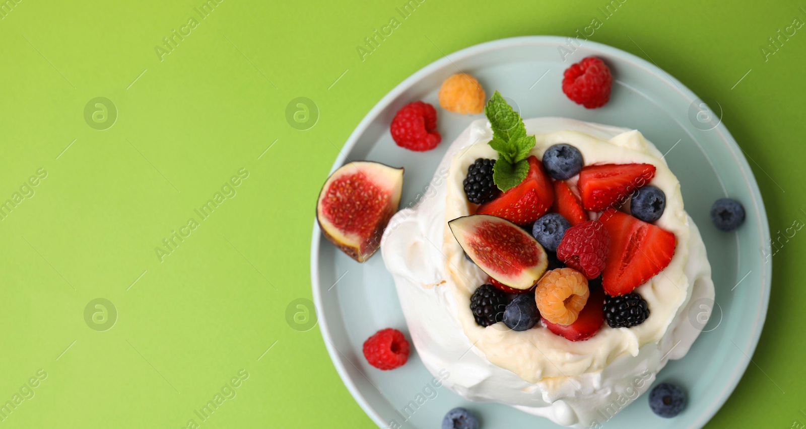 Photo of Pavlova cake (meringue dessert) with whipped cream, fresh berries, mint and fig on green background, top view. Space for text