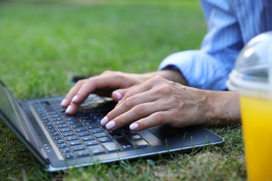 Woman using laptop on green lawn in park, closeup