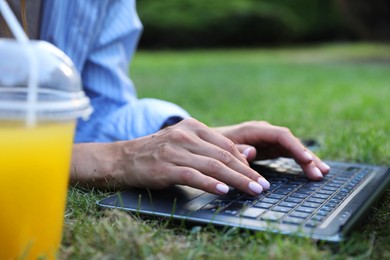 Woman using laptop on green lawn in park, closeup