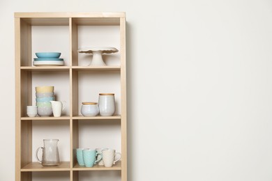 Wooden shelving unit with kitchenware on white background, space for text