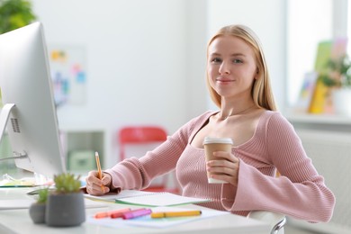 Designer with paper cup of drink working at table in office