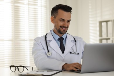 Photo of Smiling doctor working with laptop at table in clinic