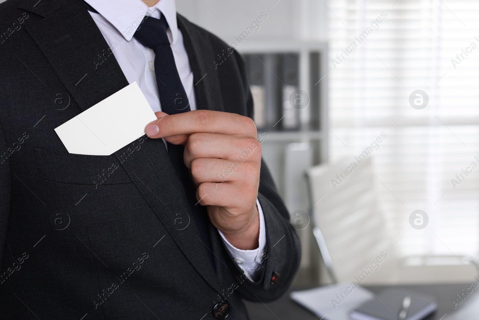 Photo of Man taking blank business card from pocket of his jacket in office, closeup. Mockup for design